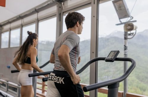 Two people running on treadmills in a gym with a mountain view, promoting fitness.