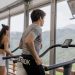Two people running on treadmills in a gym with a mountain view, promoting fitness.