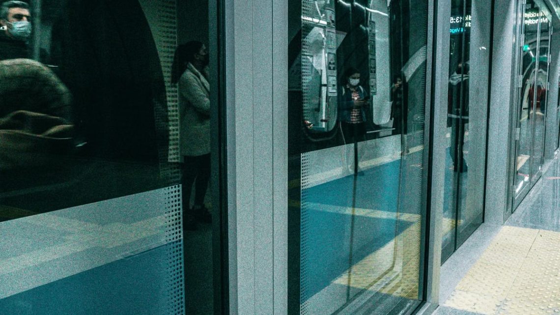 People waiting at Istanbul metro platform with reflections and modern architecture.